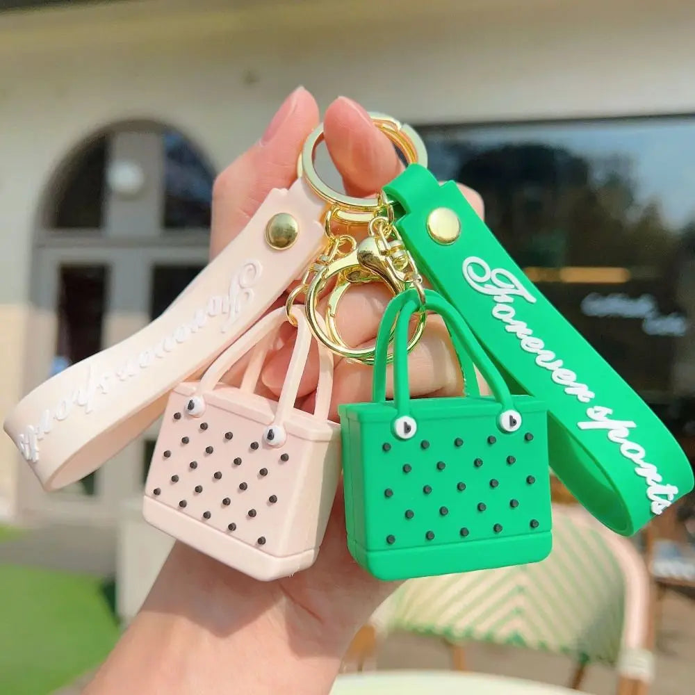 A hand holds a silicone heart beach bag keychain in pink and green colors.