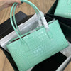 A light mint green crocodile print leather handbag is shown in a black box with tissue paper.
