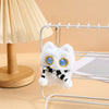 A white fluffy cat plush toy with blue eyes and a black and white striped ribbon charm hanging from a wire rack.