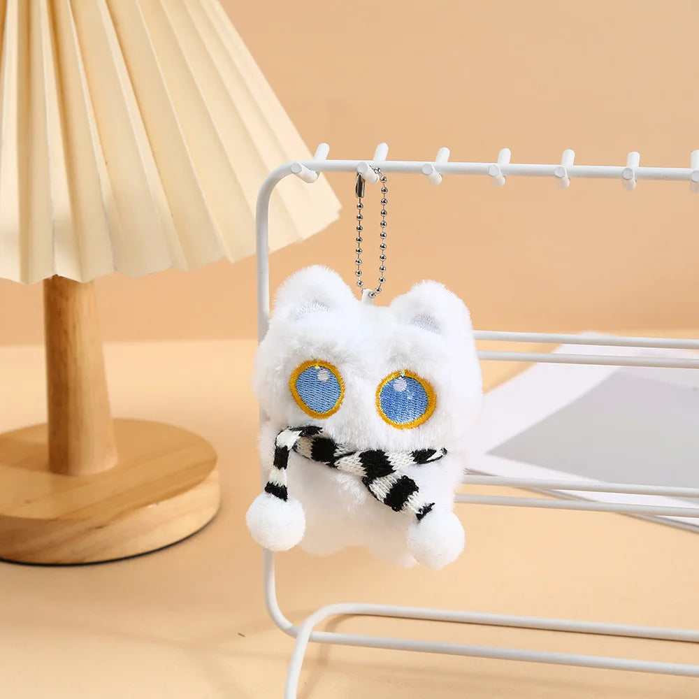 A white fluffy cat plush toy with blue eyes and a black and white striped ribbon charm hanging from a wire rack.