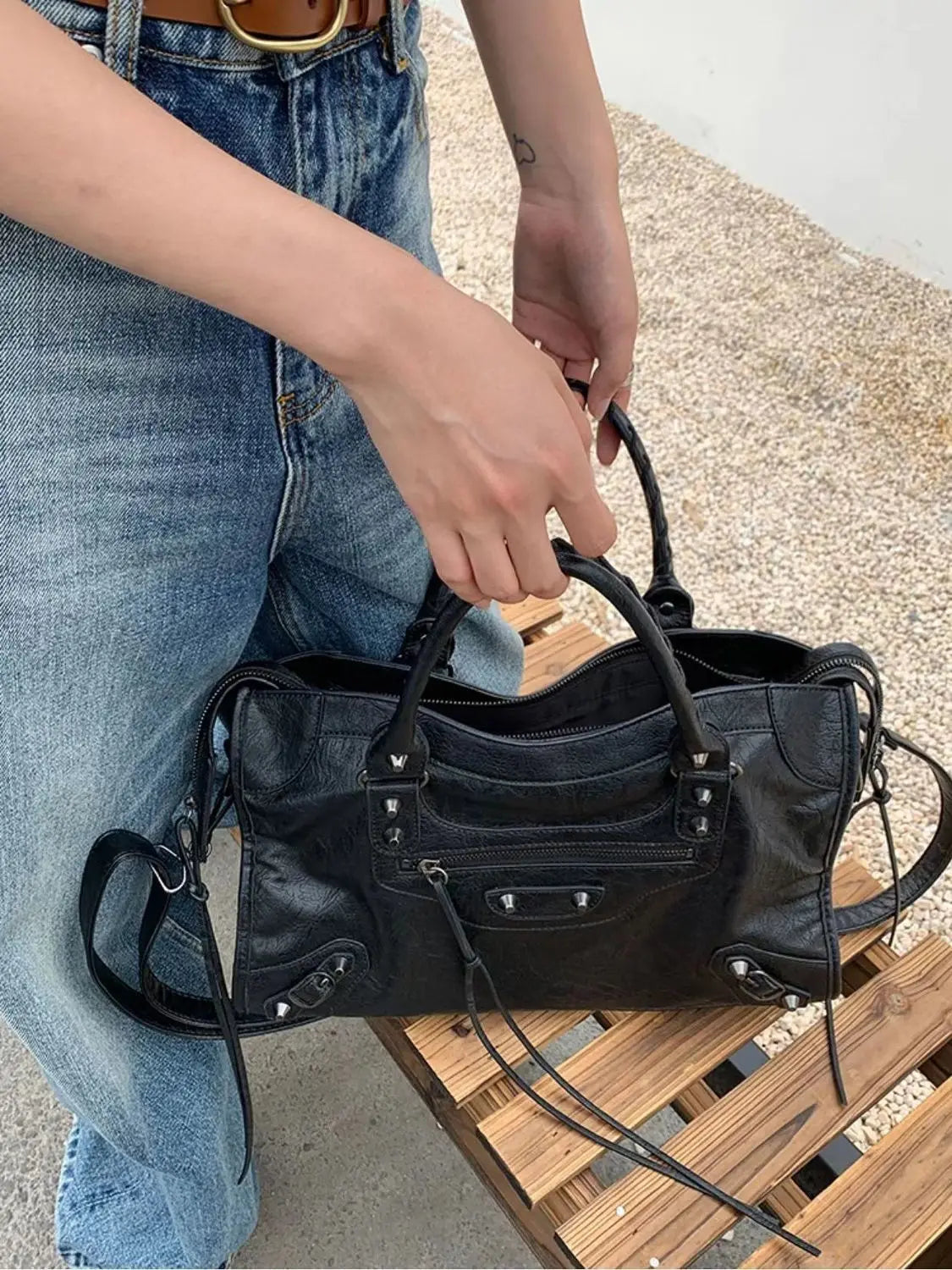 A person holds a black saddle-shaped PU leather city tote bag with black leather straps.