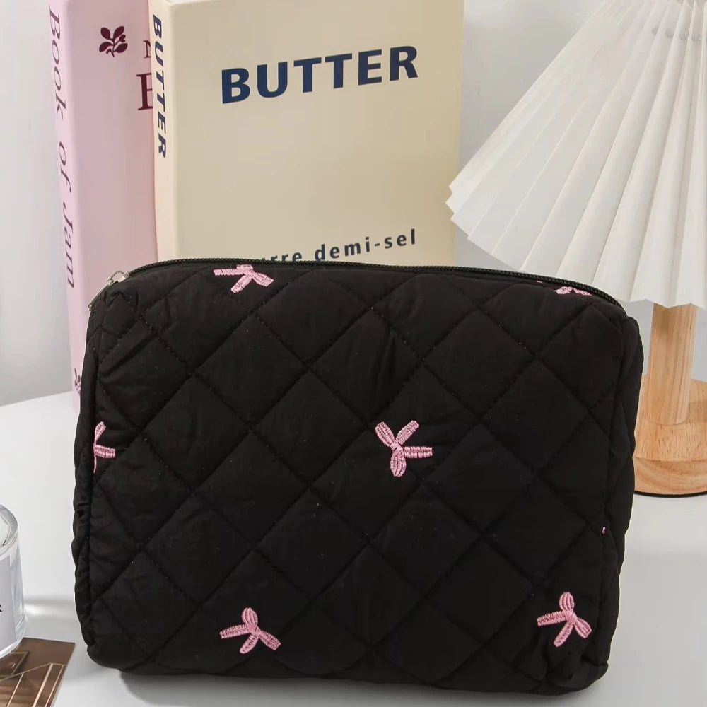 Black quilted cosmetic bag with pink bow embroidery resting on a white surface.
