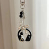 Silver music headphone keychain featuring black beads, a heart charm, and a bow detail.