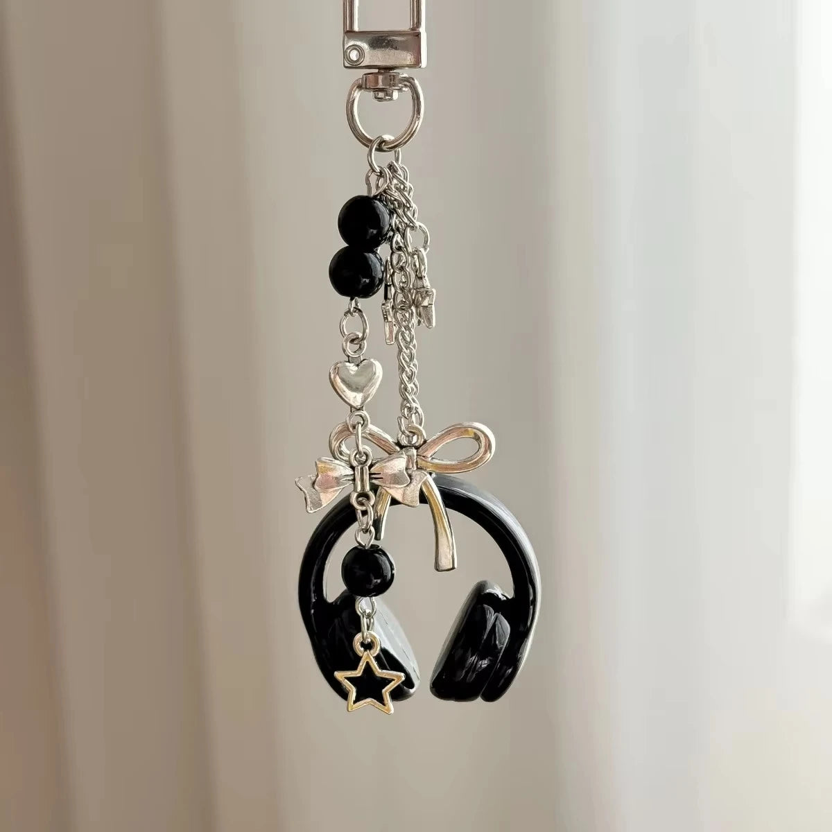 Silver music headphone keychain featuring black beads, a heart charm, and a bow detail.