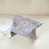 A purple floral canvas makeup bag resting on a light surface next to a photo.