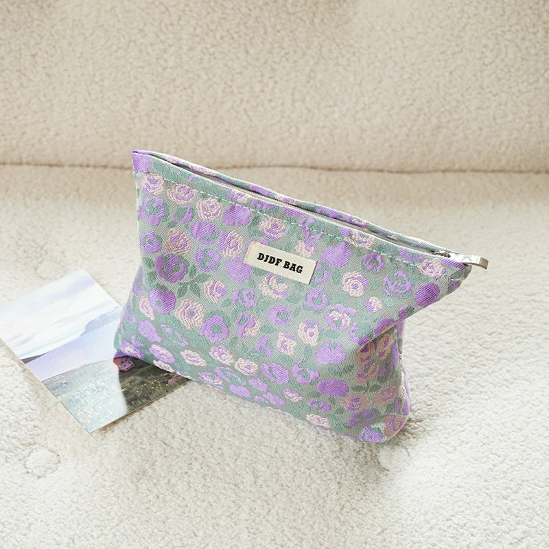 A purple floral canvas makeup bag resting on a light surface next to a photo.
