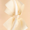 A close-up of a cream-colored satin bow headband, showing the fabric texture and knot detail.