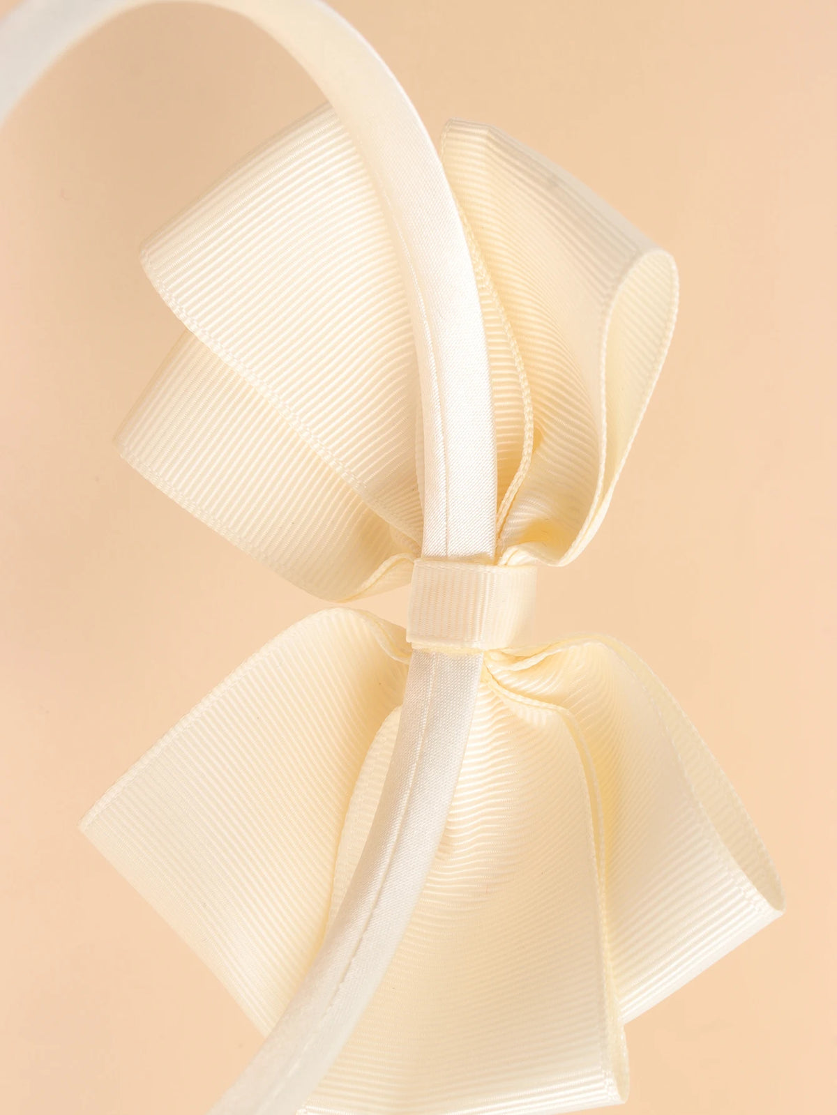 A close-up of a cream-colored satin bow headband, showing the fabric texture and knot detail.