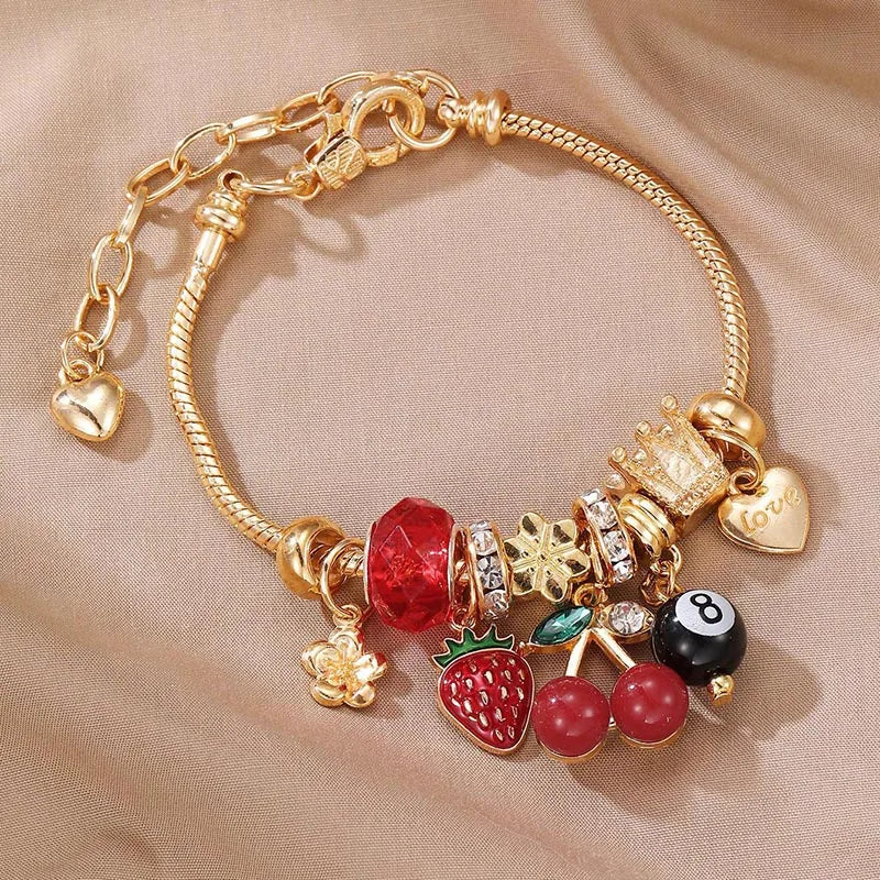 Gold chain bracelet featuring a leopard cross charm, red bead, and strawberry charm.