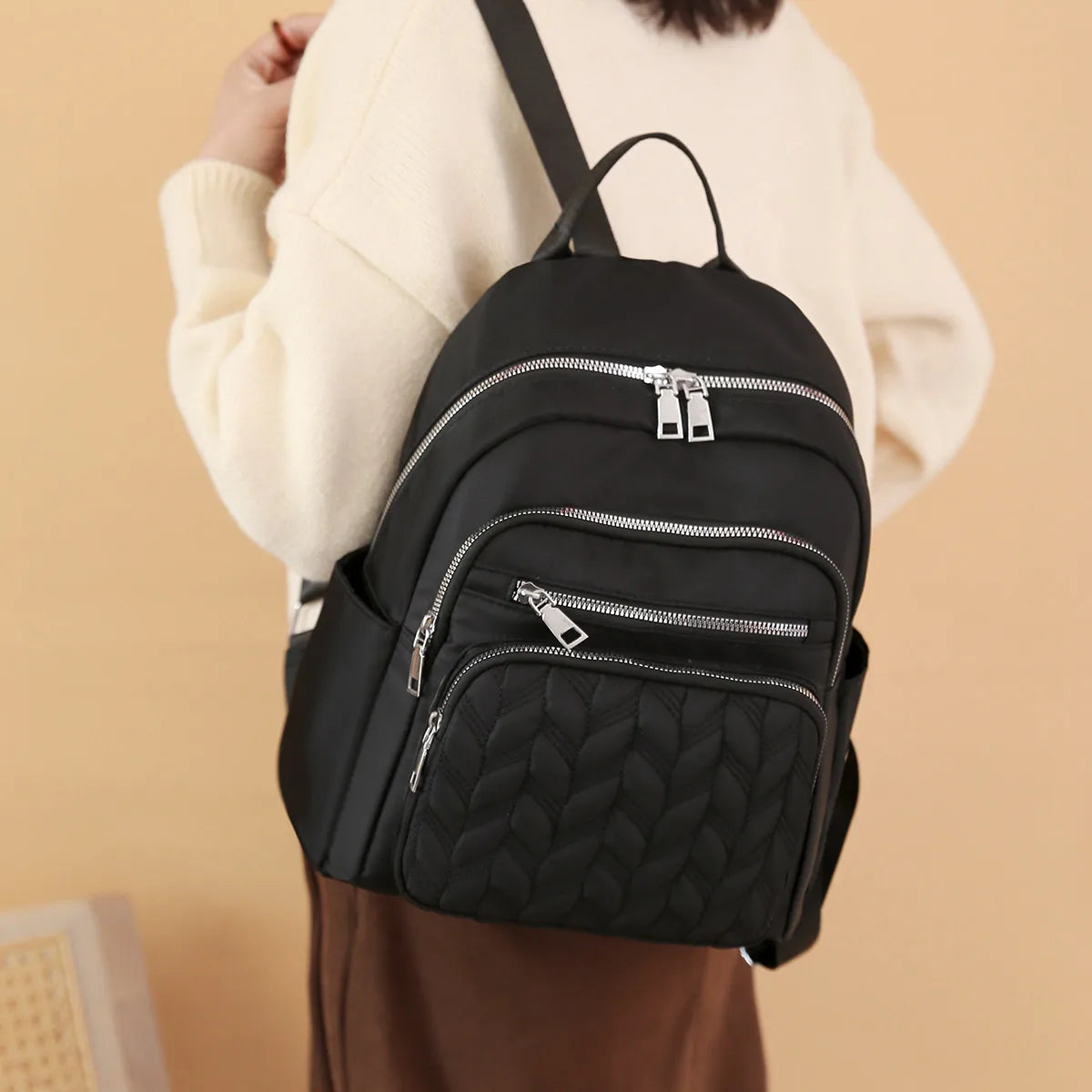 A black waterproof women's travel backpack worn by a person in a cream sweater.