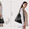 A woman models a beige blazer and white pants while holding a black handwoven faux leather tote bag.