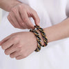 A hand is putting on a chunky gold and black Cuban link bracelet for men.