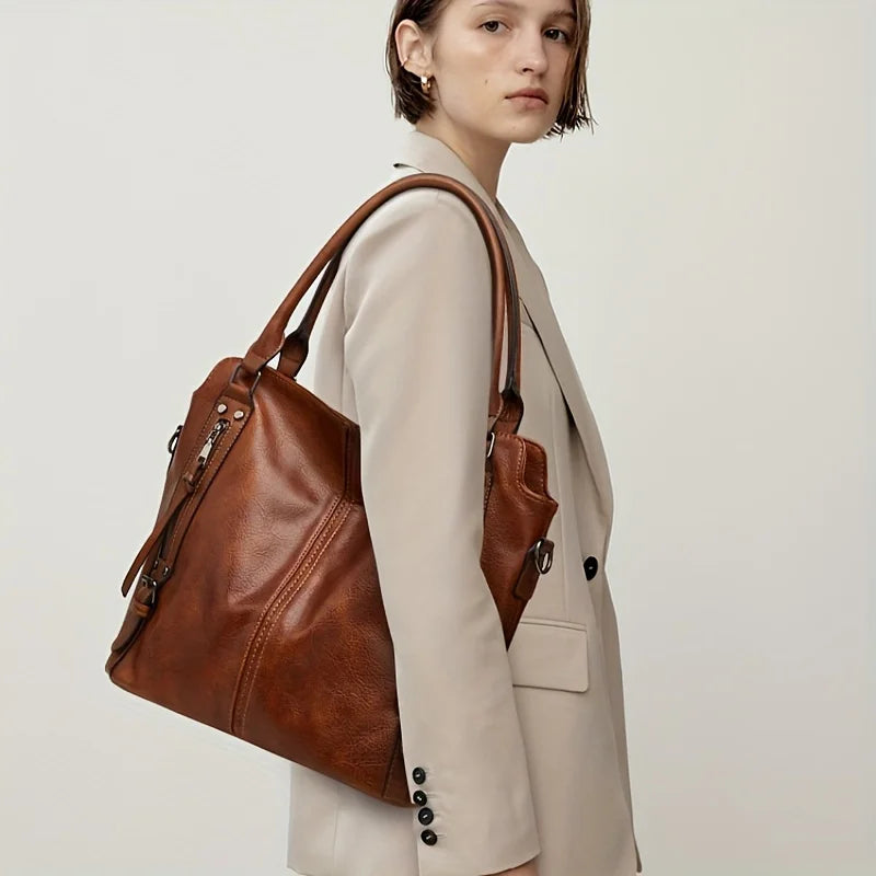 A woman wearing a beige blazer holds a brown PU leather crossbody tote bag.