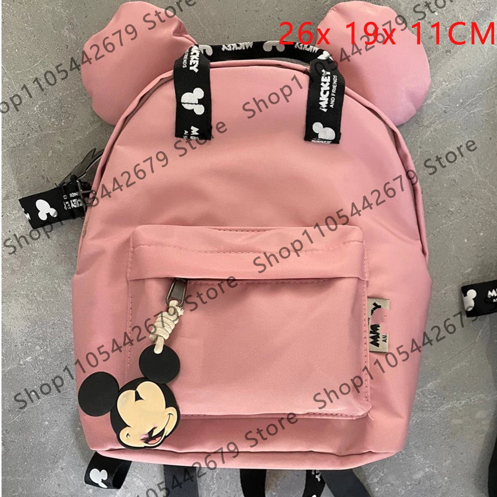 Mochila de peluche rosa con forma de ratón pato y detalles negros y un bolsillo frontal.