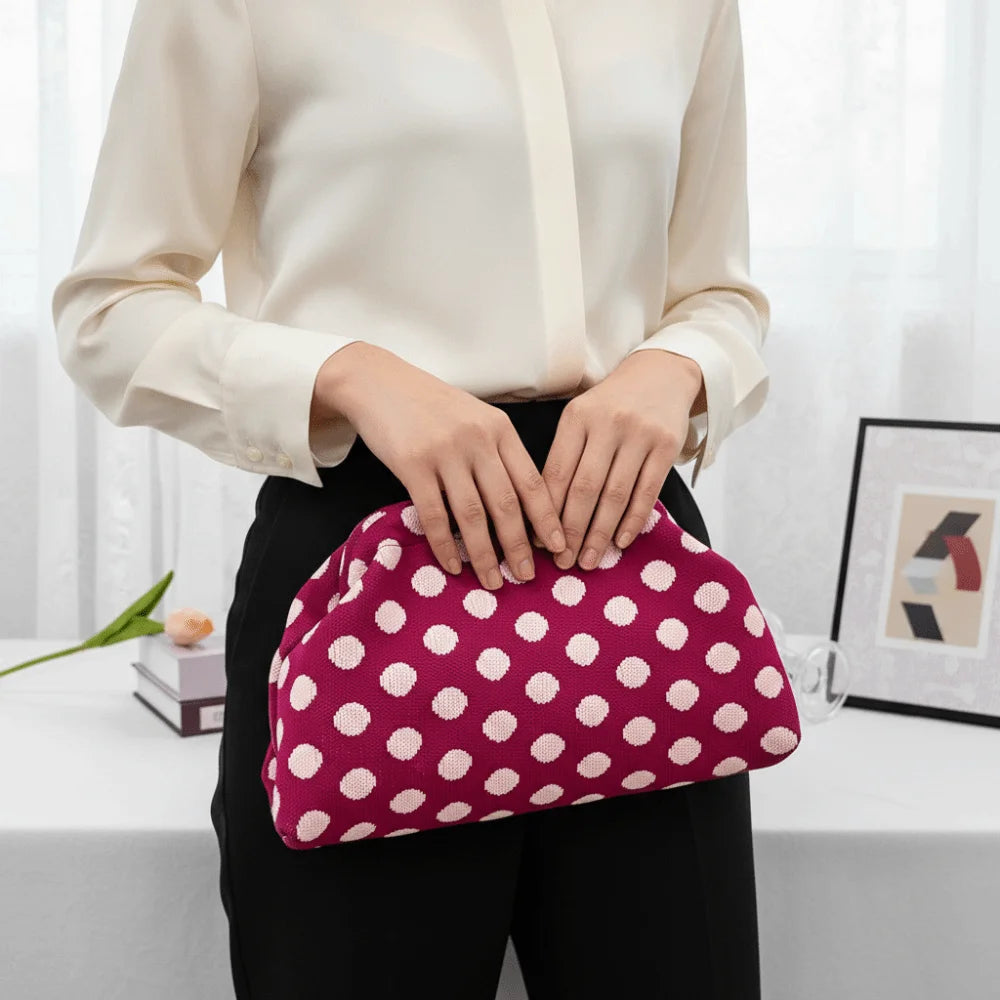 A woman holds a pink polka dot clutch bag against her black pants and white shirt.