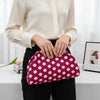 A woman holds a pink polka dot clutch bag against her black pants and white shirt.
