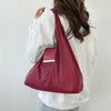A person is holding a maroon reusable nylon mini keychain tote bag with a silver rectangular charm against a white background