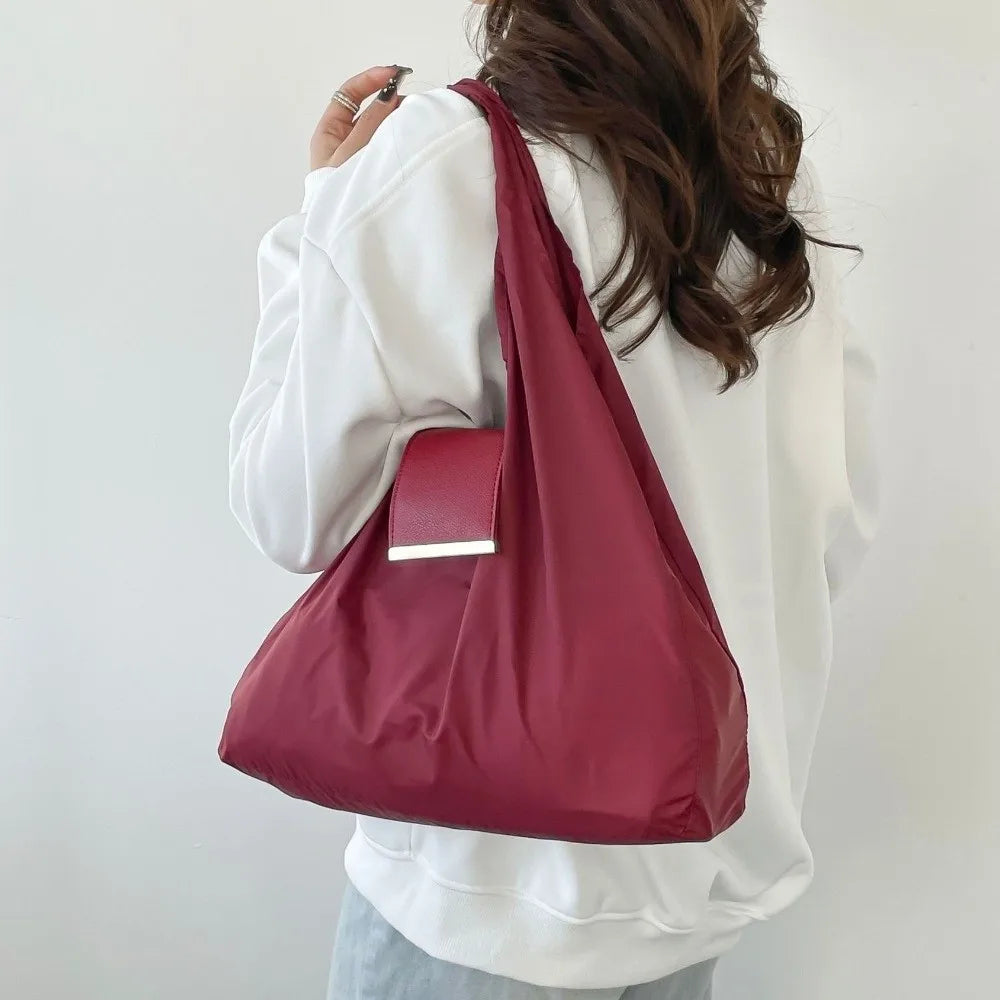 A person is holding a maroon reusable nylon mini keychain tote bag with a silver rectangular charm against a white background