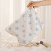 A hand holds a white cosmetic bag with a light blue starfish pattern on a soft, textured surface.