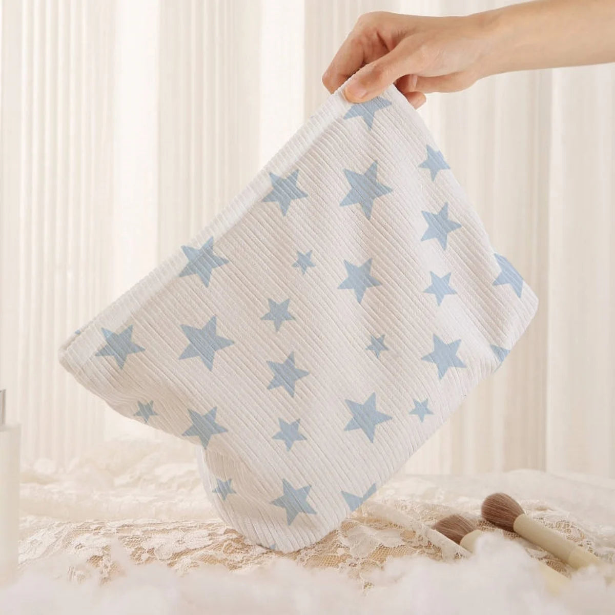 A hand holds a white cosmetic bag with a light blue starfish pattern on a soft, textured surface.