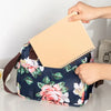 Una mano sostiene un cuaderno beige dentro de una bolsa de almuerzo floral azul marino.
