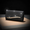 A black sequined envelope clutch with a gold chain resting on a wooden surface.
