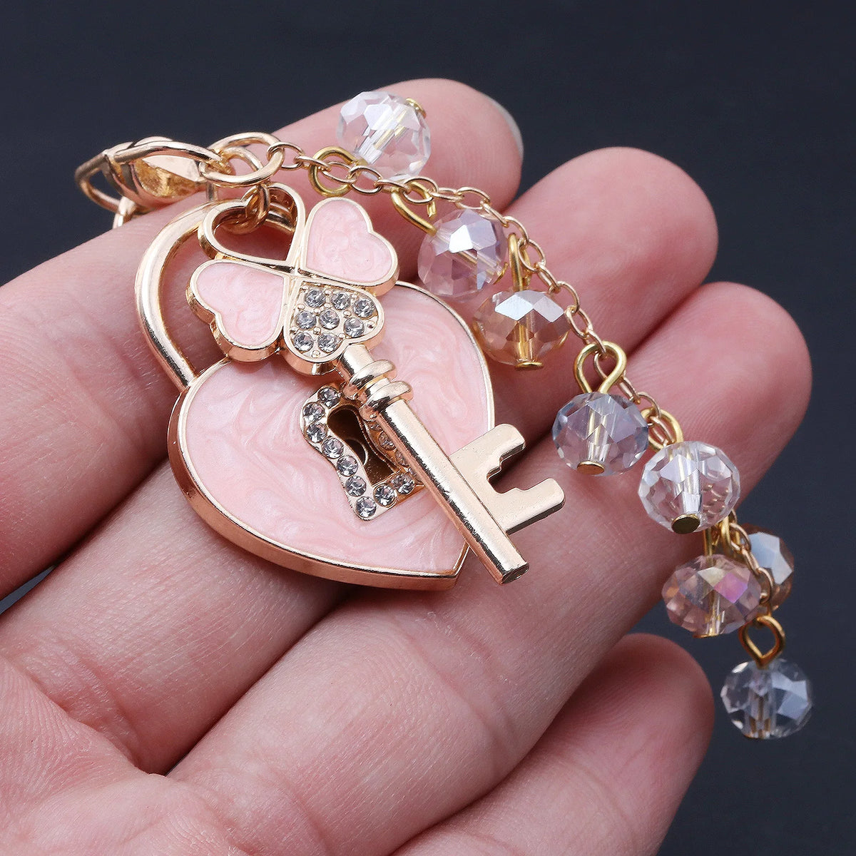 Gold-toned key chain featuring a heart and bow design with clear rhinestones and pink enamel.