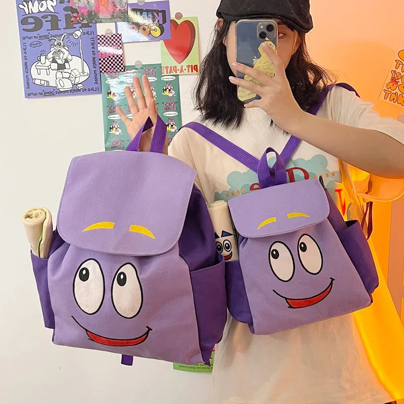 A person holds a purple Dora The Explorer cartoon flannel backpack against an orange background.