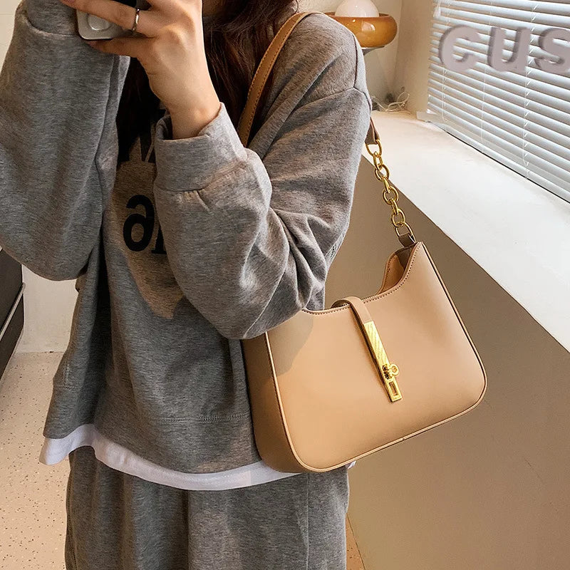 A woman holds a tan PU leather hobo shoulder bag with a gold chain against a light background.