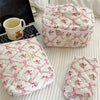 A white quilted floral embroidered makeup bag with a lid and a separate quilted pouch are displayed on a white surface.