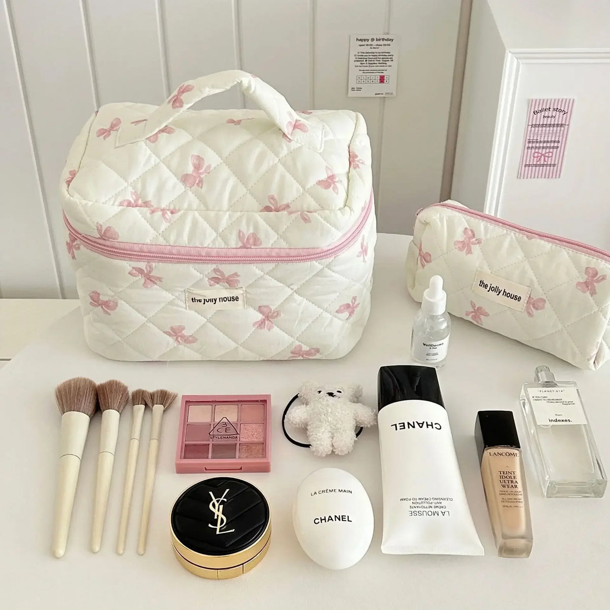Sac de rangement cosmétique en duvet blanc avec motif nœud, entouré de produits et outils de beauté.