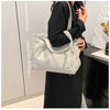 A woman holds a light gray corduroy casual handbag against a dark background.