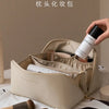 A hand is opening a beige cosmetic bag, revealing a cylindrical product inside.