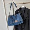 A dark blue denim tote bag with a chain strap is displayed hanging on a hanger against a light background.