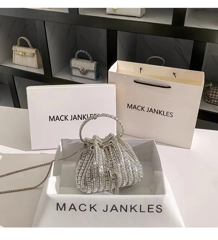 A crystal-embellished evening clutch with a chain displayed in a white box and on a marble surface.