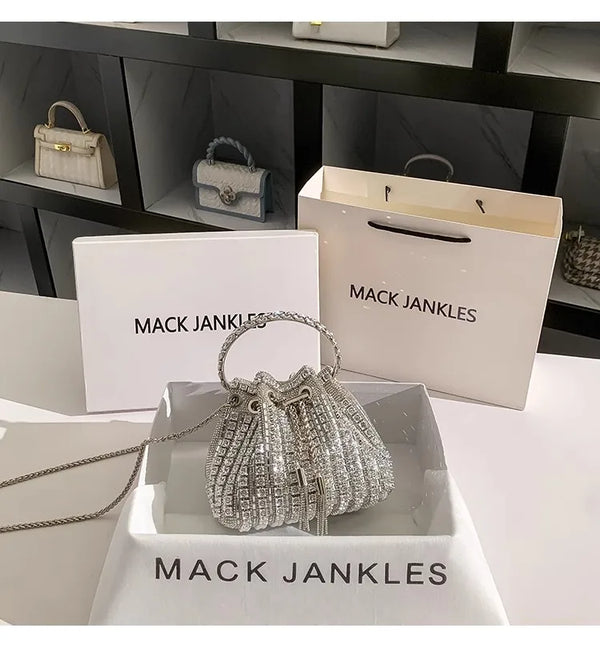 A crystal-embellished evening clutch with a chain displayed in a white box and on a marble surface.