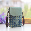 A teal denim mini messenger bag with a light green flap and brown leather strap resting on a white surface.