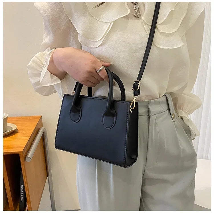 Une femme tient un sac à main en cuir PU noir minimaliste à anses supérieures sur un fond clair.