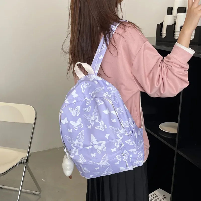 A woman is holding a light purple butterfly pattern backpack against a dark shelf.