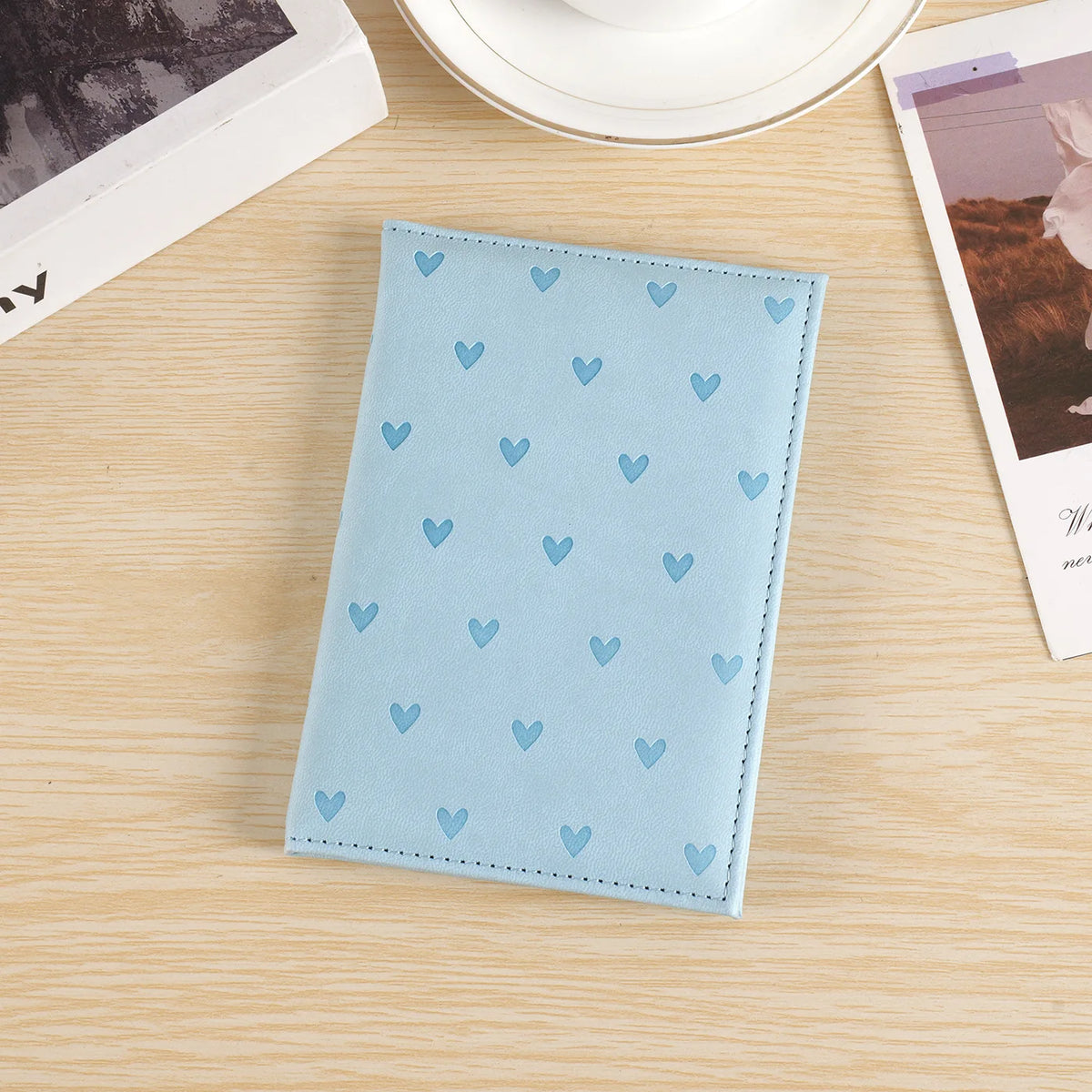Light blue heart print passport cover travel wallet for women resting on a wooden surface.
