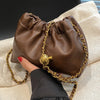 A brown PU leather chain shoulder bag is being held by a hand, resting on a light-colored fabric.