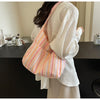 A woman holds a pink and yellow striped canvas shoulder bag against a white blouse.