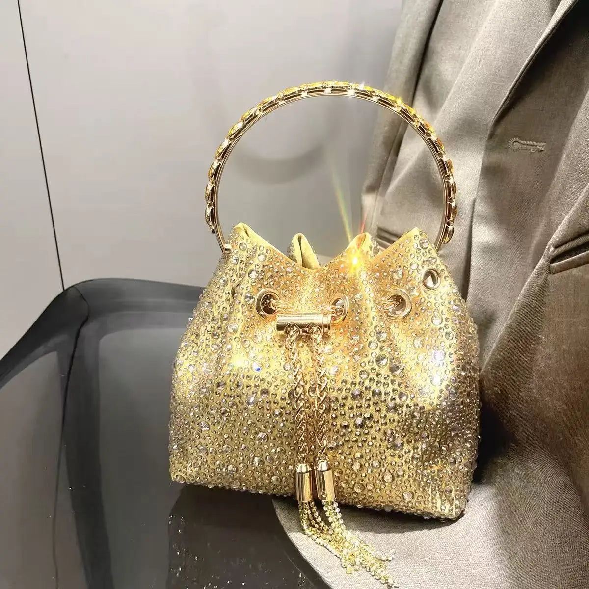A gold crystal-embellished evening clutch with a chain is displayed against a gray suit jacket.