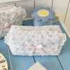 A white quilted cosmetic storage pouch with pink floral embroidery and a pink ribbon, next to a light blue ceramic cup.