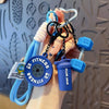 A hand holds a fitness keychain featuring a dumbbell and kettlebell charm attached to a blue cord.