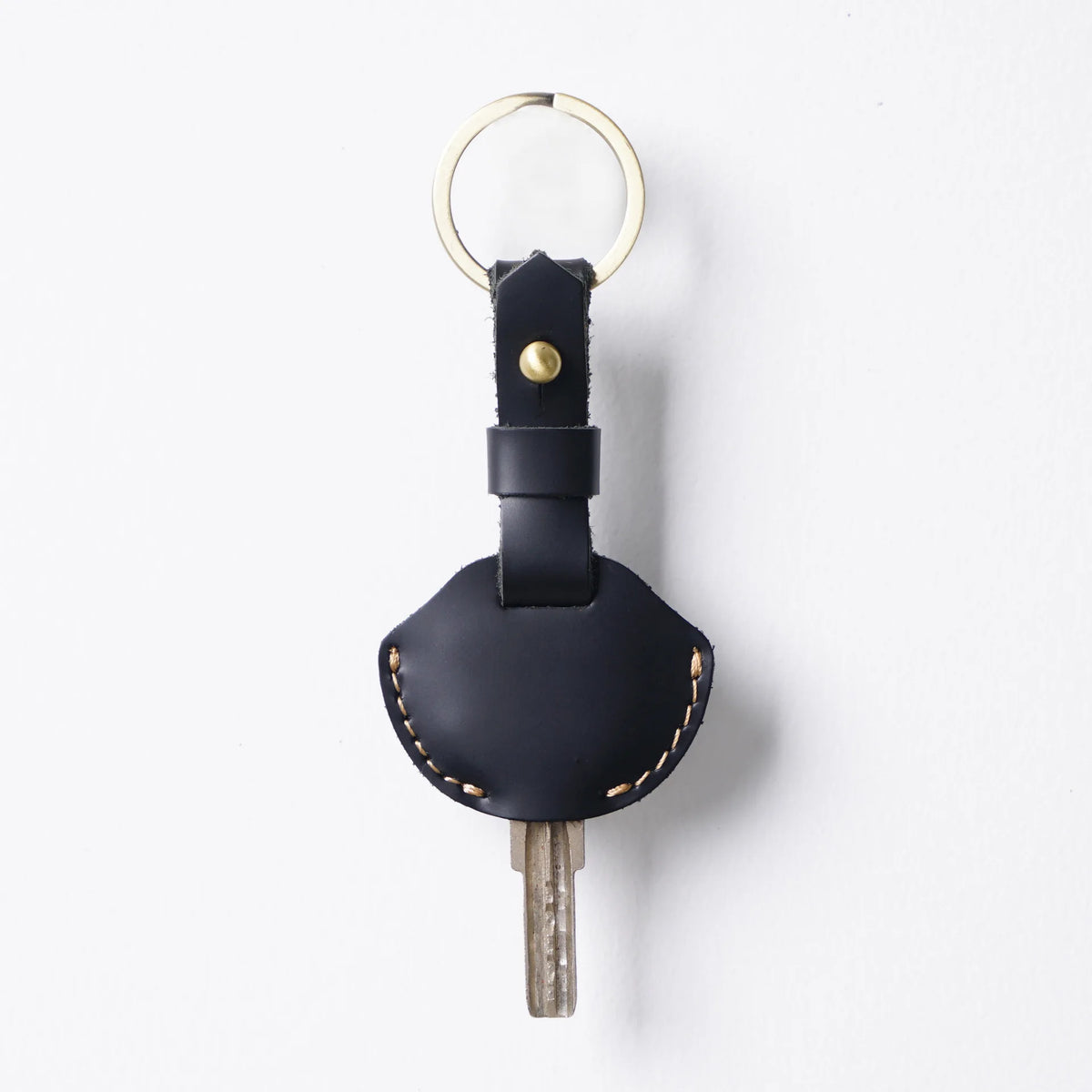 A black genuine leather key fob cover with a gold-colored ring and a metal key attached.
