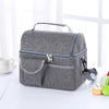 A gray reusable insulated lunch bag with a handle and zippered compartments is shown on a white surface.