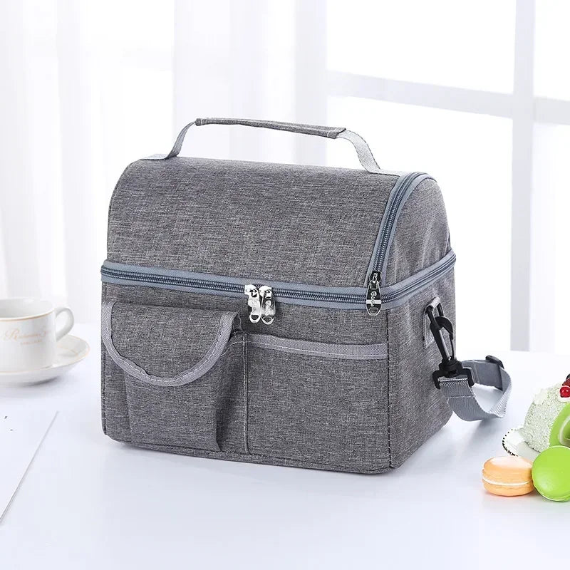 A gray reusable insulated lunch bag with a handle and zippered compartments is shown on a white surface.