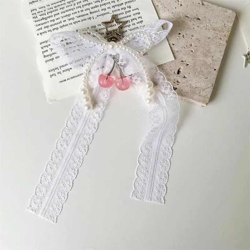 A pearl keychain featuring a bowknot design with white lace and pink beads on a white ribbon.