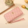 A pink patterned zipper wallet lying next to a vintage-style clock and a yellow tulip.